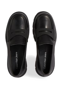 Mocassini neri in pelle caratterizzati da una fascia elastica nera testurizzata, punta arrotondata e suola rigata. Il marchio presente sulla soletta indica Calvin Klein Jeans.