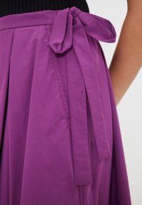 Falda plisada morada con un lazo atado en la cintura, confeccionada en una tela suave, que presenta un diseño limpio y detalles de costura sutiles.