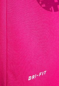 Pink Dri-FIT fabric, smooth texture, fitted design, featuring a circular pattern in a darker shade, with white lettering at the bottom.