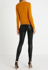 Rostfärgad stickad tröja med långa ärmar, i kombination med tajta svarta läderbyxor och svarta högklackade skor. Synlig sömdetalj på ryggen.