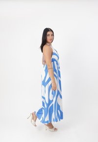 Abito lungo con un motivo astratto blu e bianco, design a collo halter, tessuto fluido e spacchi laterali. Abbinato a sandali con tacco e cinghie.