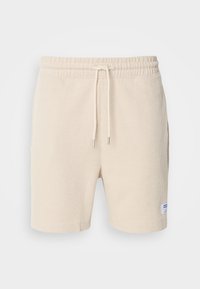 Shorts beiges en tissu texturé avec un motif en relief, dotés d'une taille élastique, d'un cordon de serrage et de poches latérales. Étiquette logo bleue.