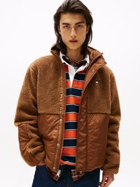 Veste en polaire marron avec une section inférieure en matelassé marron, dotée de boutons pression et d'un col haut. Portée par-dessus une chemise rayée multicolore.