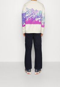 Sudadera blanca con un gráfico multicolor de montañas en púrpura y azul. Combinada con pantalones cargo azul marino oscuro y zapatos deportivos.