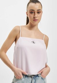 Gaiši rozā, bez piedurknēm tops ar plāniem siksniņām un kvadrātveida dekoltē. Uz krūtīm ir mazs melns logotips. Gluda auduma.