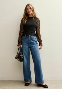 Zwart top met doorschijnende leopardenmouwen, gecombineerd met wijde blauwe jeans. Accessoires zijn een zwarte handtas en zwarte platte schoenen.