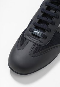 Mörk marinblå sneakers med en slät syntetisk övre, meshdetaljer, rund tå, plana snören och en märkespatch på tungan. Gummiyttersula.