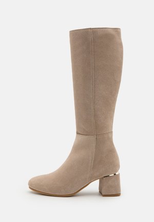 Botte beige en daim montant jusqu'au genou avec bout rond et talon bloc présentant un petit accent métallique près de la semelle.