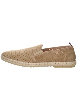 Zapato slip-on de color beige, perforado, con acentos elásticos en los laterales, suela de yute trenzado y textura suave, que presenta una punta redondeada y un perfil bajo.