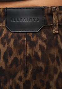 Ύφασμα με σχέδιο λεοπάρ σε καφέ και μαύρους τόνους, με μαύρο δερμάτινο ταμπελάκι με την ένδειξη «ALLSAINTS» στη μέση.