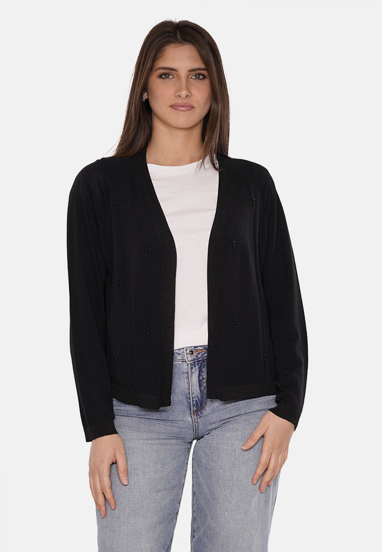 Cardigan nero con un design a maglia testurizzata, apertura frontale e dettagli in perline sottili. Indossato sopra una maglietta bianca e abbinato a jeans in denim chiaro.