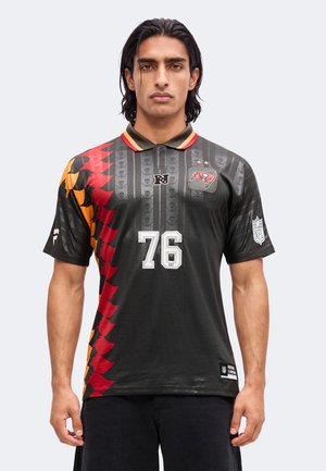 Man draagt een zwart Tampa Bay Buccaneers NFL-shirt met nummer 76 en een rood-oranje gekarteld patroon aan de linkerkant.
