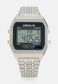 Montre numérique avec un boîtier rectangulaire en acier inoxydable, un affichage bleu et noir, un bracelet en métal argenté et des boutons pour les fonctions de lumière et de mode.