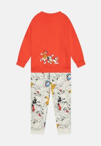 Felpa rossa con personaggi dei cartoni animati sulla schiena, abbinata a pantaloni color crema con un motivo stampato colorato a tutto campo di figure dei cartoni.