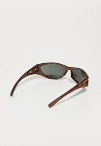 Óculos de sol castanhos com uma forma alongada e curva; lentes escuras; armações texturizadas; recortes decorativos nas laterais; hastes elegantes.