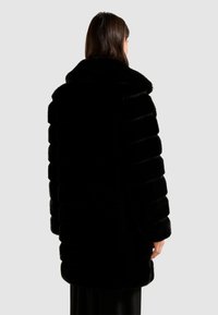 Abrigo de piel sintética negra con un cuello ancho, textura a rayas y un corte a media longitud. Presenta una superficie suave y un dobladillo redondeado.