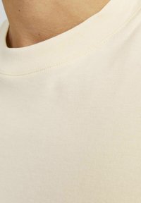Beige T-shirt met korte mouwen, voorzien van een ronde hals, een gladde textuur en contrasterende stiksels langs de halslijn.