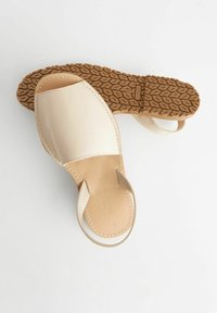 Sandali in pelle beige con punta aperta, parte superiore morbida e suola in gomma marrone testurizzata con motivo a foglia.