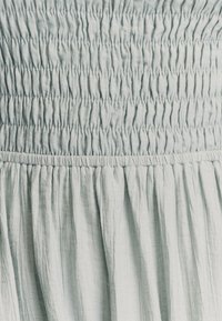 Svetlomodrá zhromaždená látka s textúrovaným, pokrčeným povrchom. Obsahuje elastický nariasený dizajn, ktorý vytvára prúdiaci a uvoľnený vzhľad.