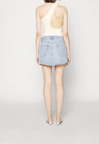 Hellgelbes, geripptes Bodysuit mit asymmetrischem Ausschnitt, kombiniert mit einem denim Minirock in Hellblau mit ausgefranster Saum. Weiße, verstellbare High-Heels-Sandalen.