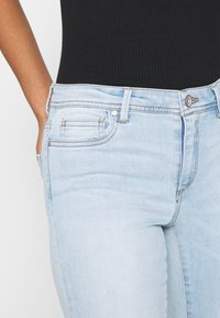 Vaqueros de mezclilla azul claro con un ajuste entallado, que incluyen un diseño clásico de cinco bolsillos, costuras sutiles y un cierre de botón en la cintura.