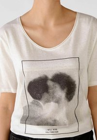 Hvid kortærmet T-shirt med sort grafik af to ansigtet, der kysser, med prikket mønster og teksten "JEG VIL KYSE DIG FOR EVIGT" nedenfor.