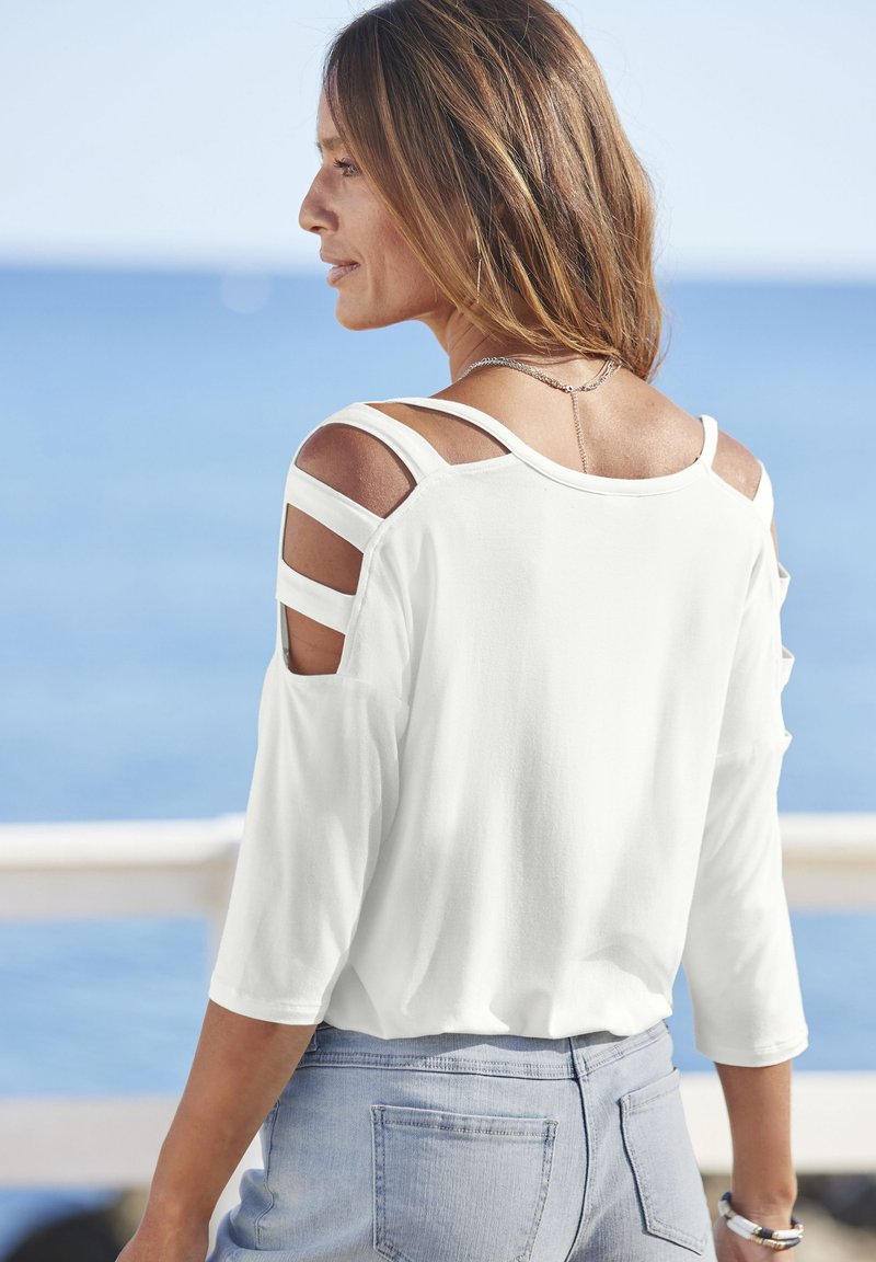 Witte lange mouwen top met een open schouderontwerp en uitsparingen. Zachte stof, relaxte pasvorm, gecombineerd met lichtblauwe denim broek.