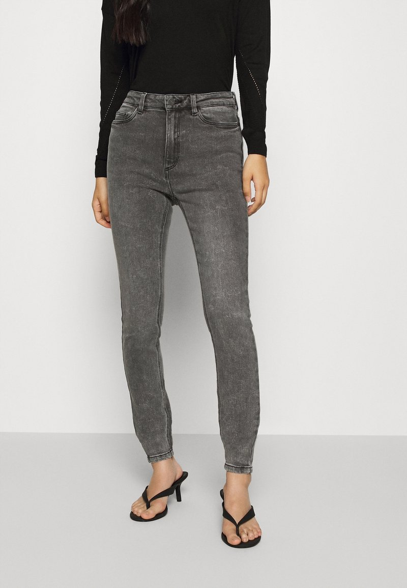 Jeans grises de talle alto con una silueta ajustada, hechos de mezclilla, con una textura suave y bolsillos frontales, combinados con chanclas negras.