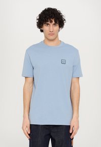 Tricou din bumbac de culoare albastru deschis, cu guler rotund și mâneci scurte. Dispune de un mic patch cu logo de culoare albastru închis pe partea stângă a pieptului. Textură moale.