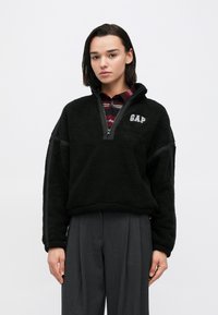 Pullover in pile nero con mezza zip e logo "GAP" ricamato. Presenta una vestibilità comoda e una superficie testurizzata per calore e comfort.