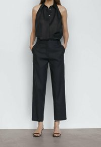 Haut en lin noir à col licou avec une fermeture à boutons sur le devant, associé à un pantalon noir large taille haute et des sandales noires à brides.