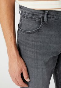 Szare dżinsy o dopasowanym kroju, z przednią kieszenią i zapięciem na guzik. Materiał ma subtelną teksturę i delikatne wyblaknięcie.