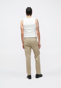 Pantaloni beige in cotone con gamba dritta, abbinati a una canotta bianca senza maniche. Presentano tasche sul retro e sono indossati con scarpe nere.