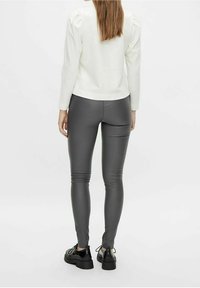 Figurbetonte graue Leggings mit glatter Textur, kombiniert mit einem weißen Langarmshirt. Schwarze Schnürschuhe mit einer breiten Sohle.