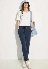 Marineblauwe joggingbroek met een koord, gecombineerd met een effen wit T-shirt en een lichtblauwe denim bucket hat, accessorized met een tote bag.