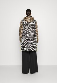 Chaqueta tipo chubasquero con capucha que presenta un estampado de leopardo en la parte superior y un patrón de cebra en blanco y negro en la parte inferior; rematada con acentos en amarillo neón.