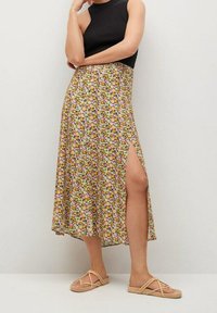 Falda midi floral en amarillo con acentos en púrpura y verde, con una abertura lateral. Combinada con una blusa negra sin mangas y sandalias ligeras.