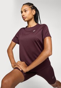 Camiseta deportiva en color burdeos con mangas cortas y un escote redondo, combinada con pantalones cortos a juego. La tela parece suave y ajustada.