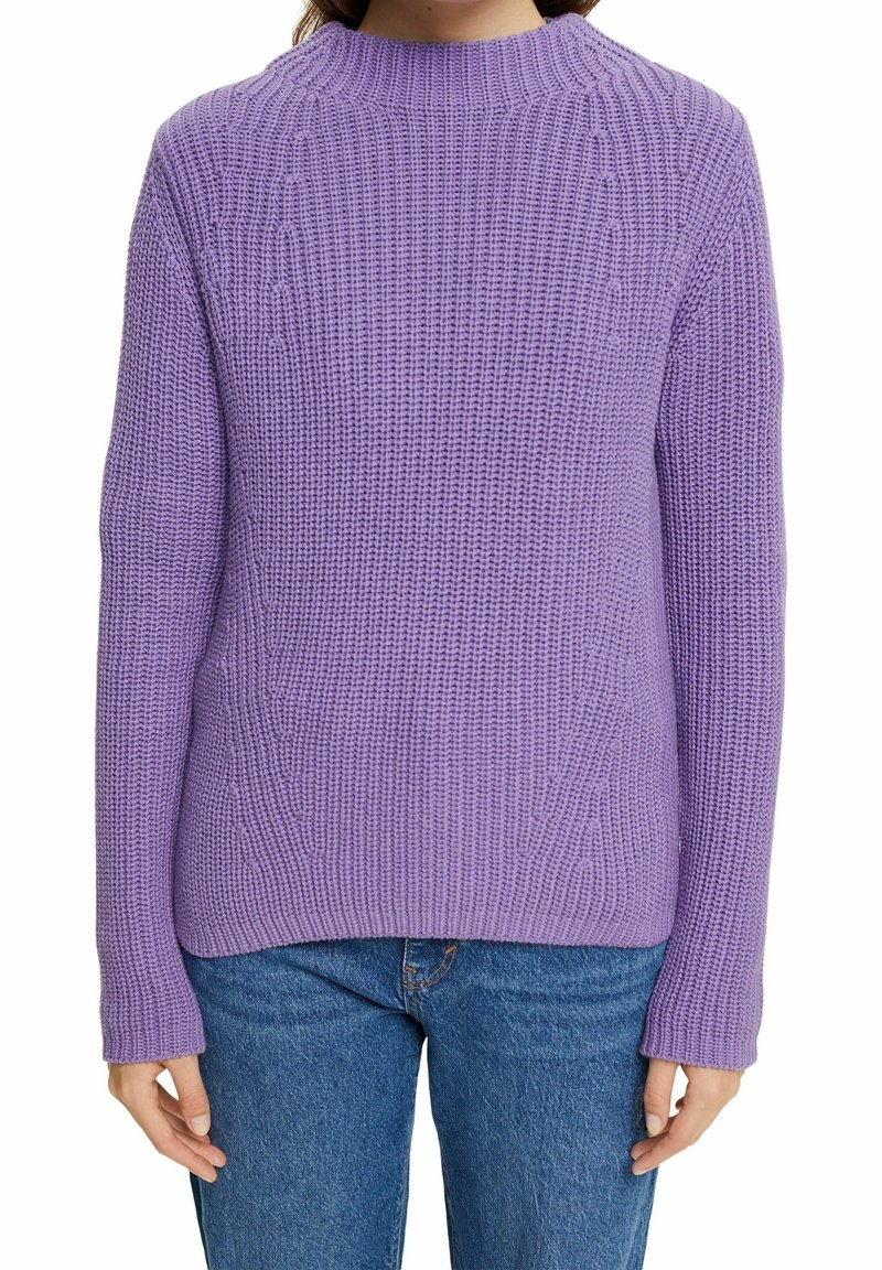 Personne portant un pull en laine lavande texturé et un jean bleu, bras détendus le long du corps, sur fond blanc.