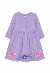 Fialové šaty s dlhým rukávom, biele bodky, drevené gombíky a farebná výšivka dinosaurov na okraji, so zátiším kvetov a zelene.