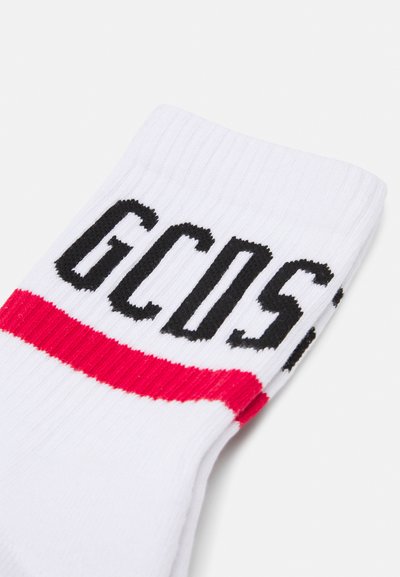 Chaussettes blanches côtelées avec une épaisse bande rouge et un lettrage noir en gras "GCOS" sur le côté. Matériau doux avec un ajustement confortable.