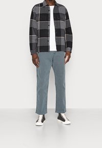 Musta- ja harmaaruudullinen kauluspaitatakki, jossa kaksi rintataskua, yhdistetty vaaleansinisiin suoralahkeisiin farkkuihin ja mustiin tennareihin, joissa valkoiset yksityiskohdat.