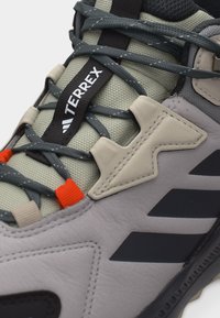 Κοντινή λήψη ενός γκρι παπουτσιού πεζοπορίας με μαύρες και μπεζ λεπτομέρειες, λεπτομερείς κορδόνια και το λογότυπο Terrex στη γλώσσα.