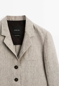 Veste beige en mélange de lin avec un col à revers cranté, deux boutons noirs et une poche poitrine. L'étiquette indique « Massimo Dutti, Fabriqué au Portugal ».