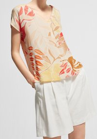 Blomstret top i let stof med V-hals og kortærmer i nuancer af orange, gul og creme. Sammen med hvide shorts.