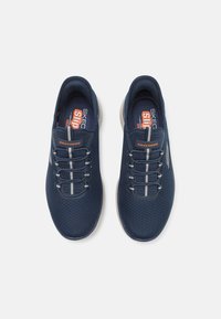 Baskets de sport bleu marine avec une tige en maille texturée, des lacets élastiques et des semelles de couleur claire. Présente le logo "Skechers" sur le côté.