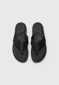 Juodai flip-flop'ai su formuotu guminiu padu ir audiniu tarpikliu, kuriame yra iškilnios logotipo detalės. Lygus dizainas, minimalus tekstūroje, ir srauni išvaizda.