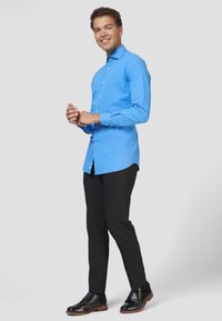 Camicia azzurro chiaro a maniche lunghe con taglio dritto, abbinata a pantaloni neri e scarpe nere, caratterizzata da una superficie di tessuto liscia.