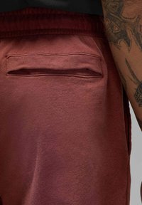 Bordeauxfarbene Sweatpants mit weicher Textur, ausgestattet mit einer Rückentasche mit horizontalem Einstieg. Der Bund ist elastisch für eine bequeme Passform.