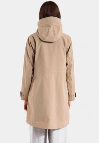 Beige vedenpitävä huppari, keskipitkä malli, pitkät hihat ja joustavat resorit, sileä pinta ja minimalistinen yksityiskohtien käyttö.